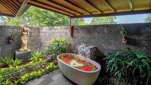 A covered outdoor area with a large bathtub filled with colorful flowers, a statue, and various plants. - The Acala Shri Sedana (Lembongan Island)