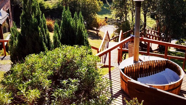 Een houten jacuzzi op een terras met uitzicht op een tuin en gebouwen in de verte.