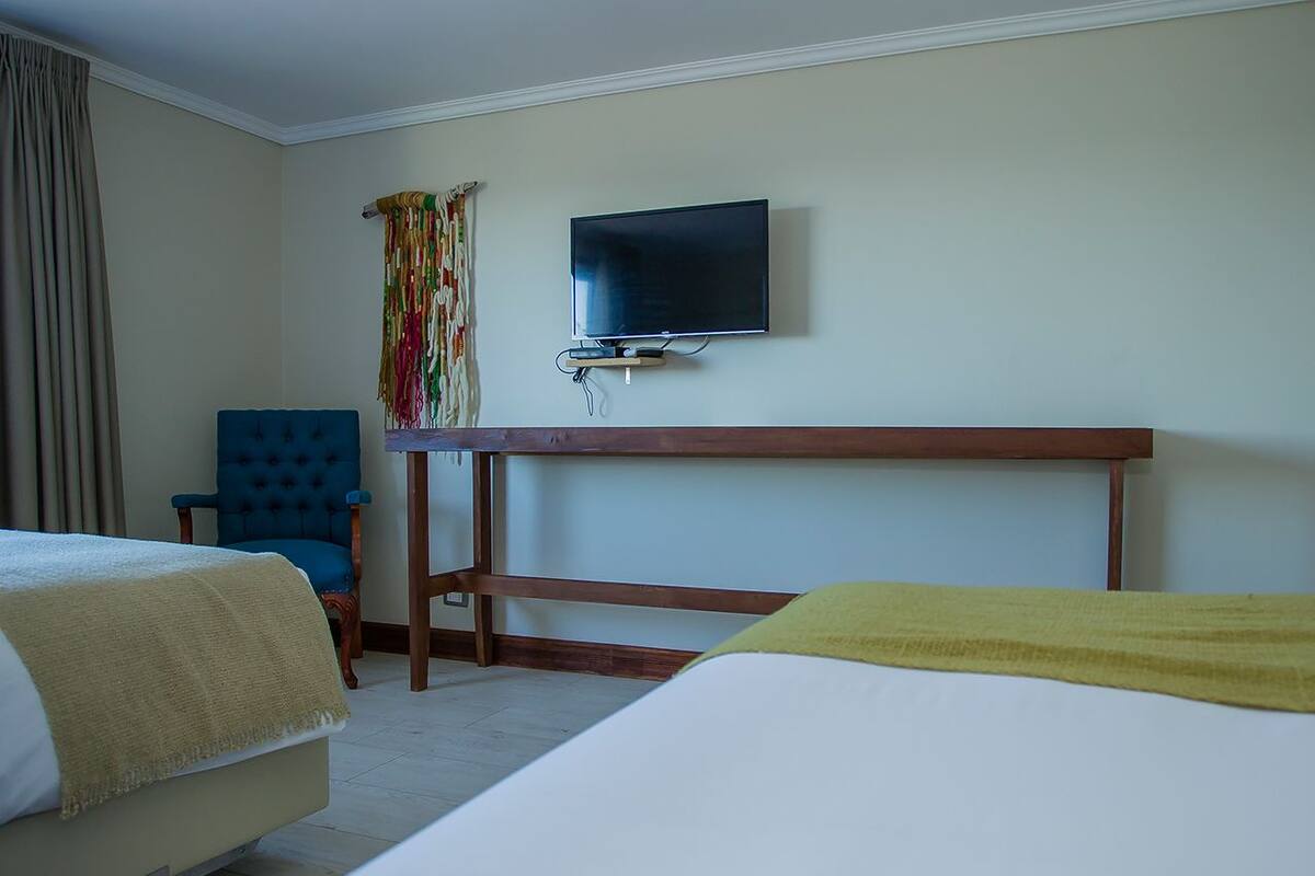 Ein Hotelzimmer mit zwei Betten, einem an der Wand befestigten Fernseher, einem Schreibtisch und einem Stuhl.