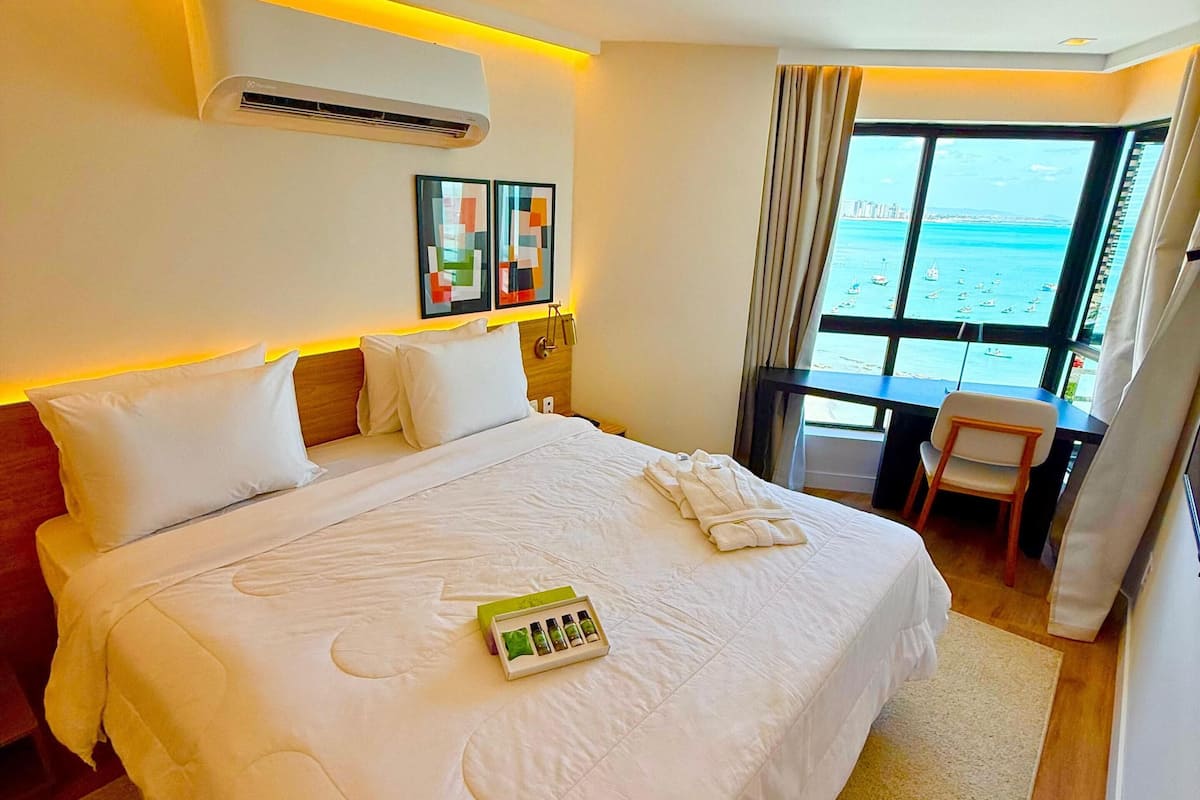 Ein Hotelzimmer mit einem großen Bett, einem Schreibtisch und Meerblick.