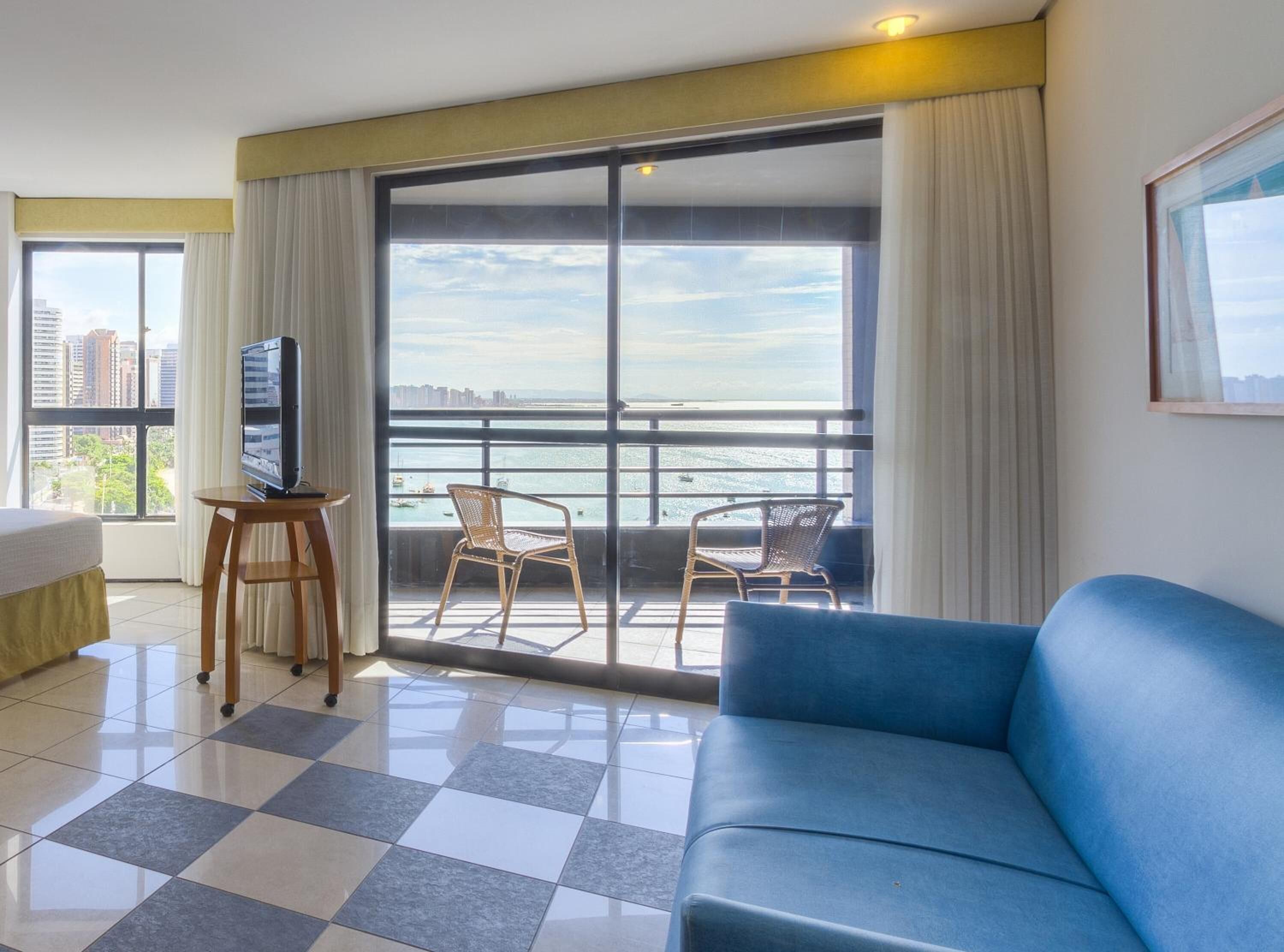 Une chambre d’hôtel avec un grand balcon, un téléviseur posé sur une petite table, un canapé bleu et un lit.