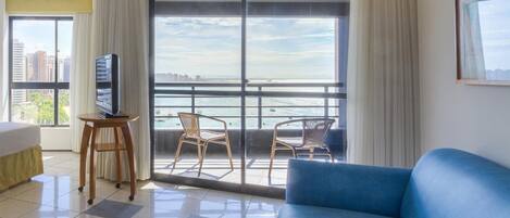 Une chambre d’hôtel avec un grand balcon, un téléviseur posé sur une petite table, un canapé bleu et un lit.