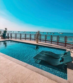 Una piscina con vista al mar, una terraza de madera y sillones de descanso.