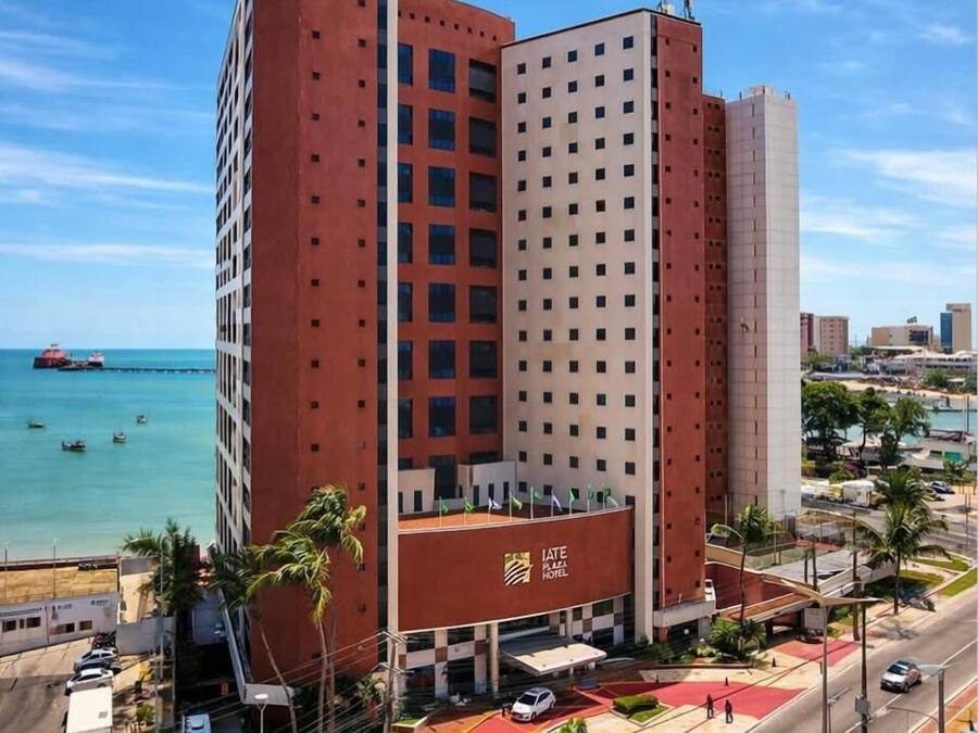 Un hotel a più piani con una facciata importante in rosso e bianco, situato all'incrocio con la costa, dove si vedono strade e veicoli.