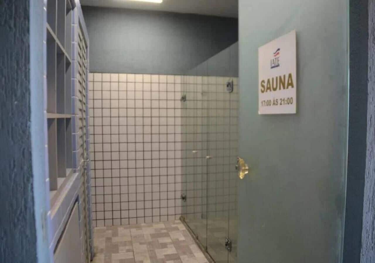 Ett duschutrymme med glasväggar, kaklat golv och en skylt som visar när bastun är öppen.