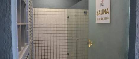 A glass-enclosed shower area with a tiled floor and a sign indicating the sauna hours.