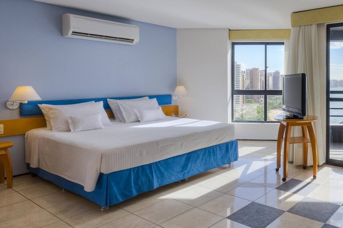 Ein Hotelzimmer mit Bett, Fernseher und Fenster mit Blick auf die Stadt.