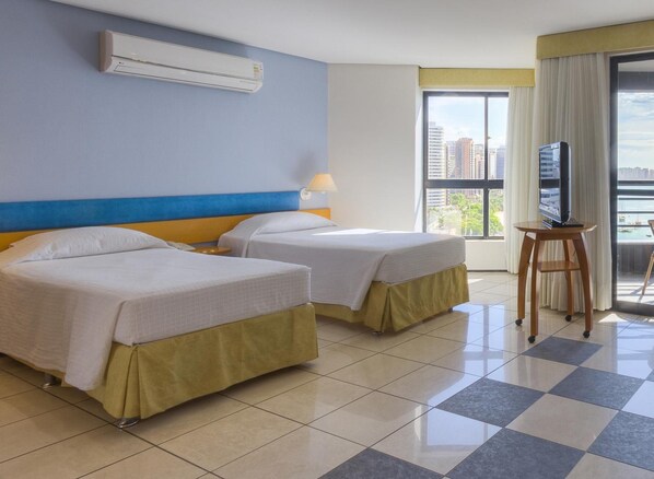 Habitación de hotel con dos camas, un televisor sobre una mesita y un ventanal con vistas a la ciudad.