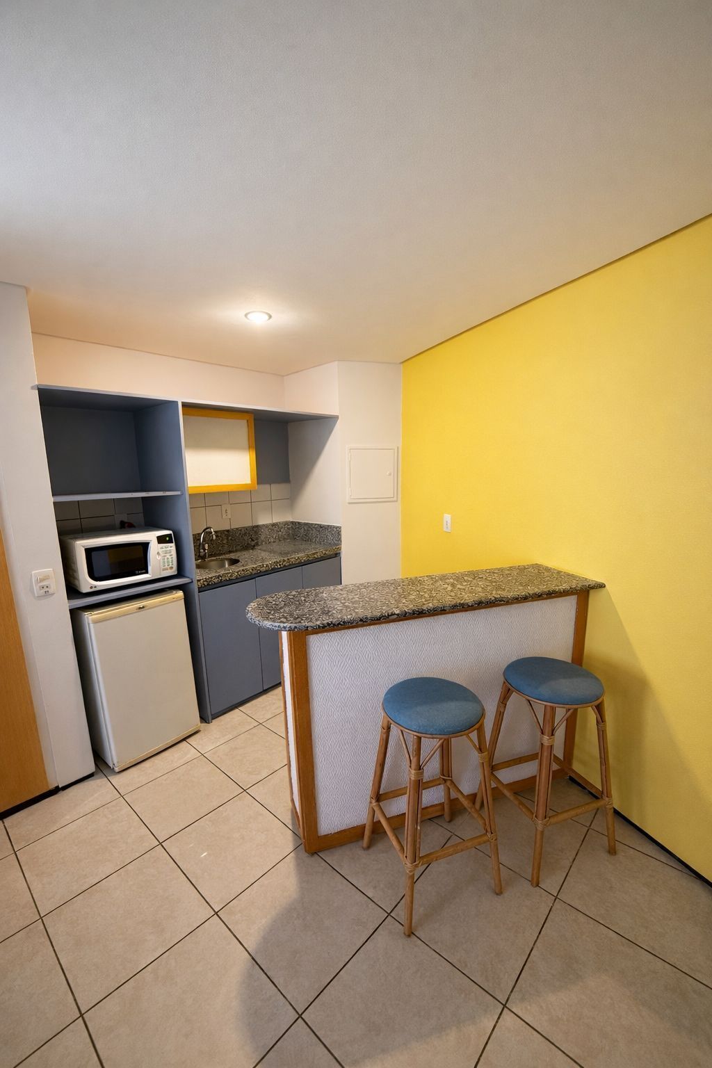 Uma cozinha compacta com micro-ondas, geladeira e uma pequena ilha com banquetas.