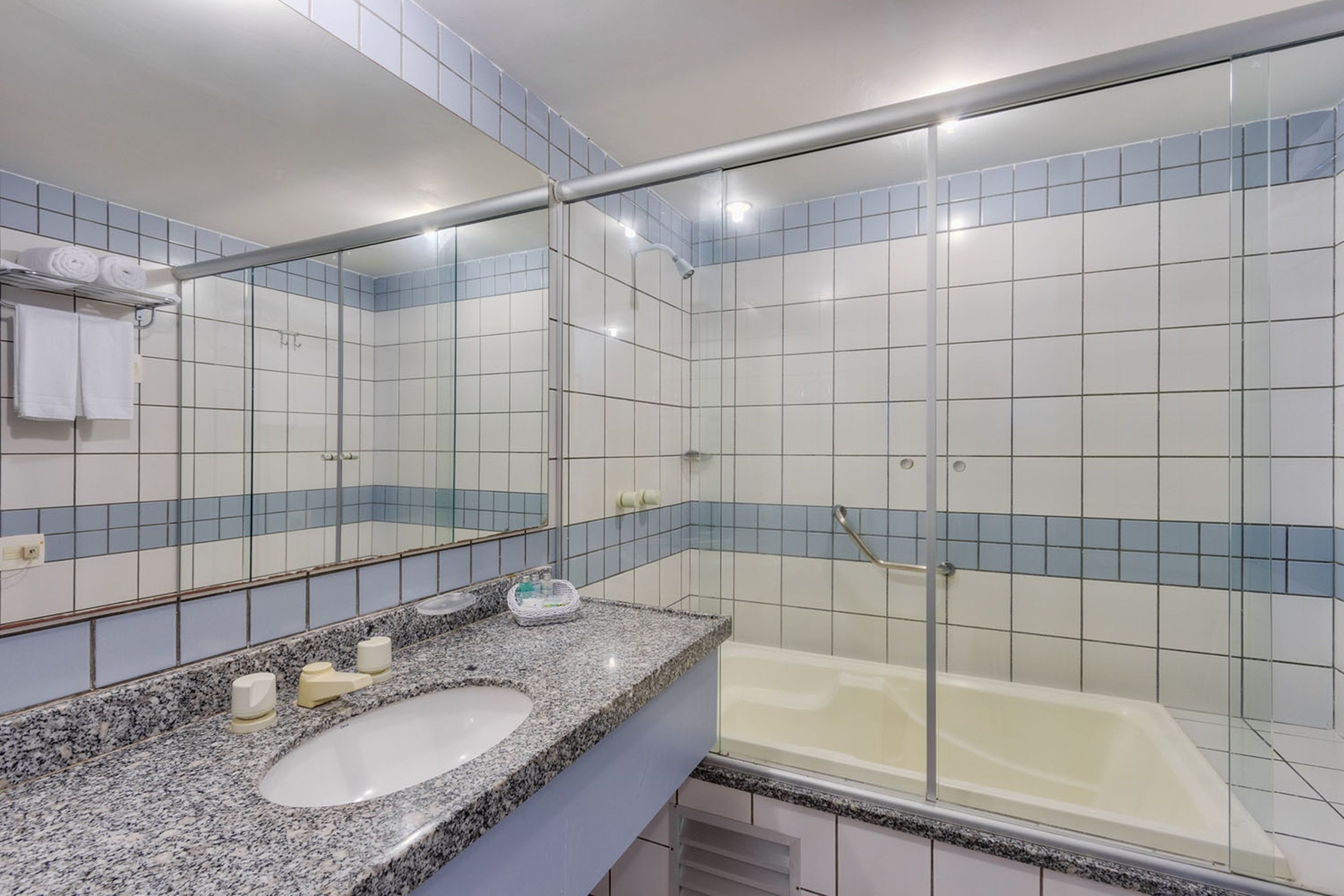 A bathroom with a granite countertop, a white sink, a glass-enclosed shower, and blue-tiled walls.