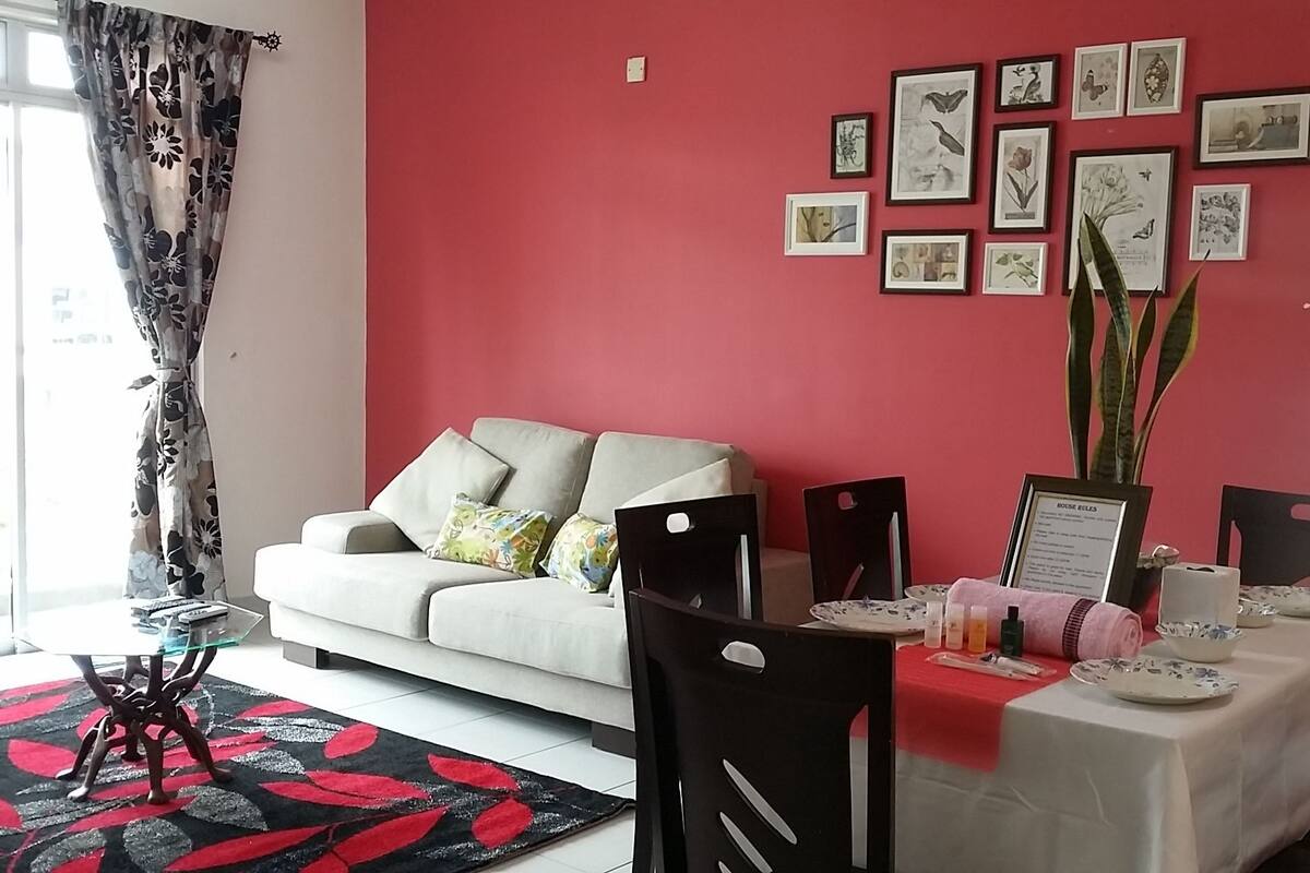 Ein Wohnzimmer mit einem weißen Sofa, einem Esstisch mit roter Tischdecke und einer Bildergalerie an der Wand.