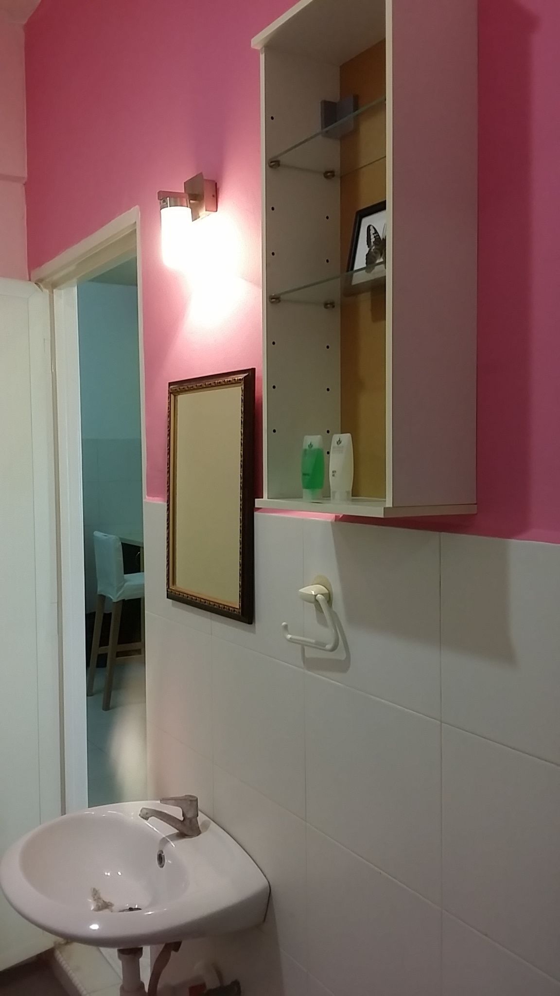 A bathroom with a white sink, a mirror, and a shelf with toiletries.