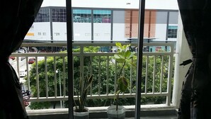 A balcony with potted plants, a view of a parking area, and a building with large windows and a sign. - Family Suite DESA TEBRAU JOHOR BAHRU (Johor Bahru)