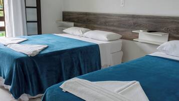 Habitación de hotel con dos camas, cada una con cubrecama azul y almohadas blancas, cabecera de madera, mesita de noche pequeña y mesita auxiliar blanca.