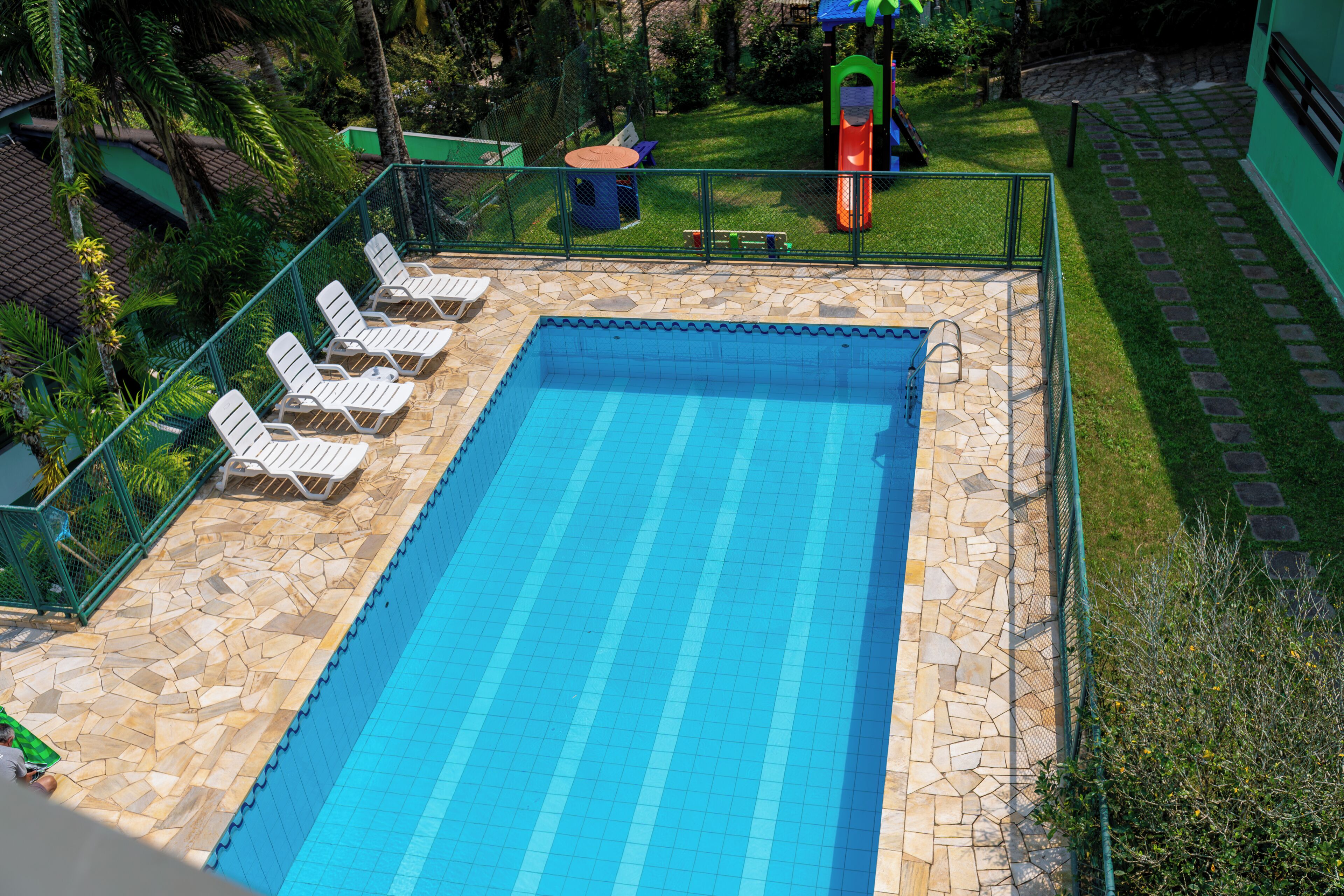 A rectangular swimming pool with a tiled edge, surrounded by a stone deck and a metal fence.