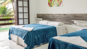 Habitación de hotel con dos camas, cabecero de madera, ventana con vista a palmeras y un cuadro de flores en la pared.