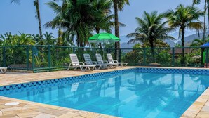 Piscina con sillas de descanso y una sombrilla verde, rodeada de palmeras y un cielo despejado.