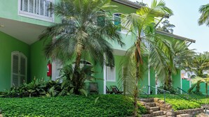 Un edificio verde con extintor, palmeras y mesas al aire libre.