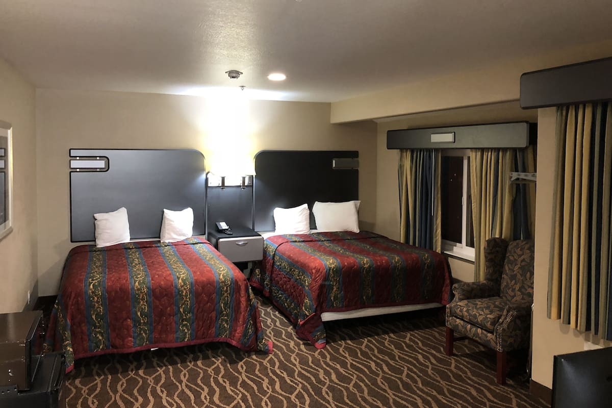 Une chambre d’hôtel avec deux lits, un bureau, une chaise et une fenêtre avec des rideaux.