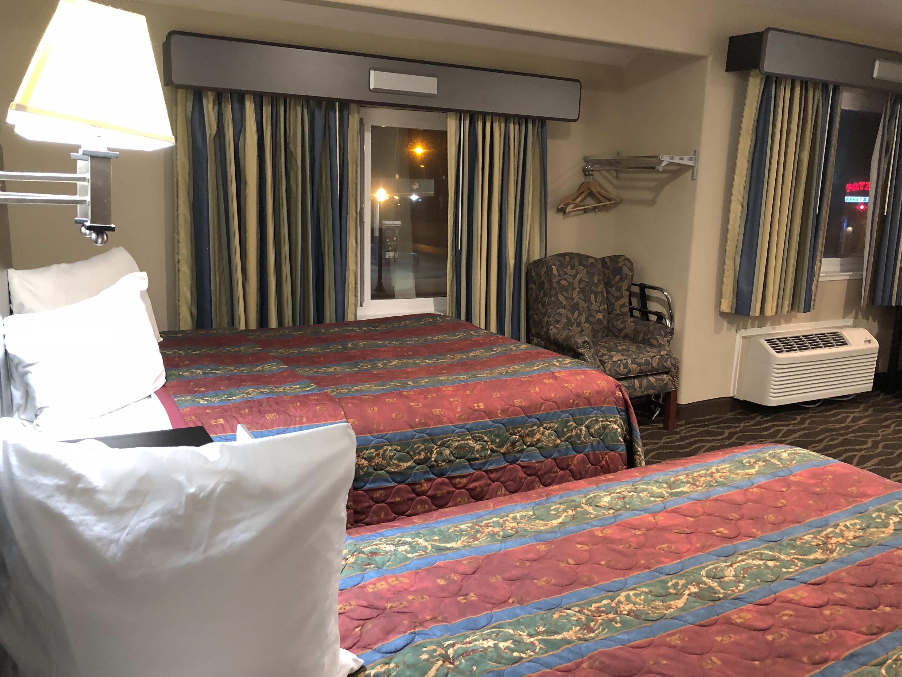 Een hotelkamer met twee bedden, een stoel, een lamp en een raam met gordijnen.