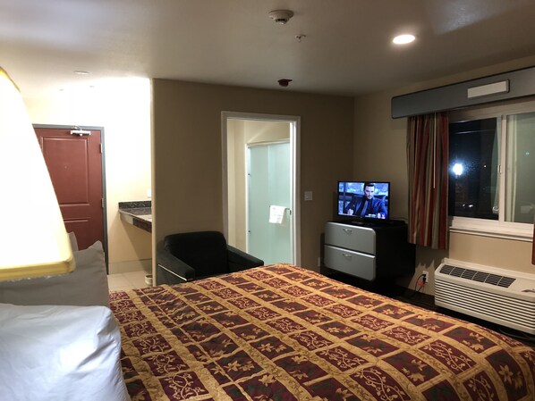 A hotel room with a bed, a desk, a television, and a window with curtains.