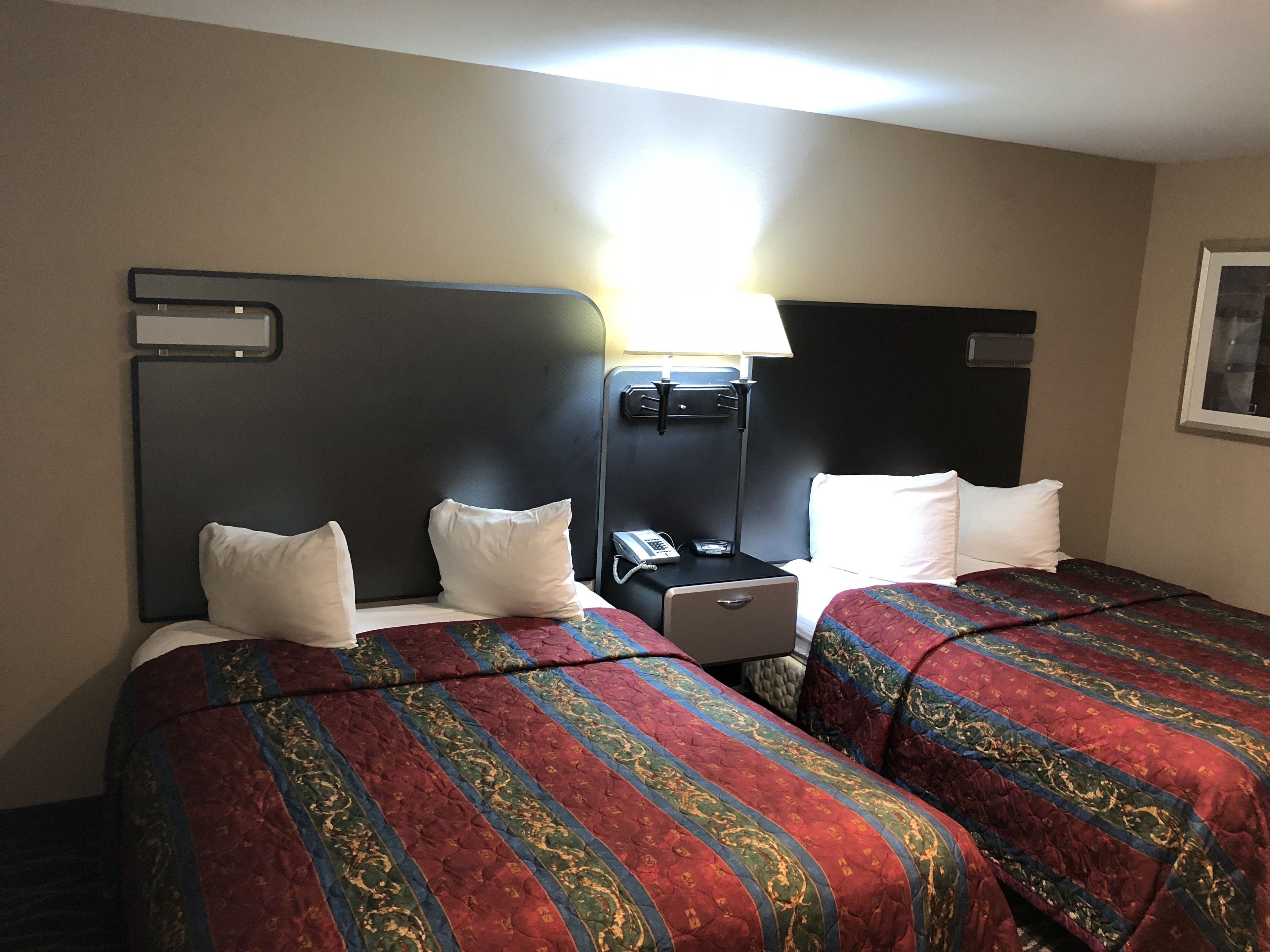 Quarto de hotel com duas camas, cada uma com colcha estampada, mesa de cabeceira com telefone e luminária.