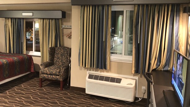 A hotel room with a patterned carpet, a chair, an air conditioning unit, and a television. - Casa Royal Inn (San Jose)