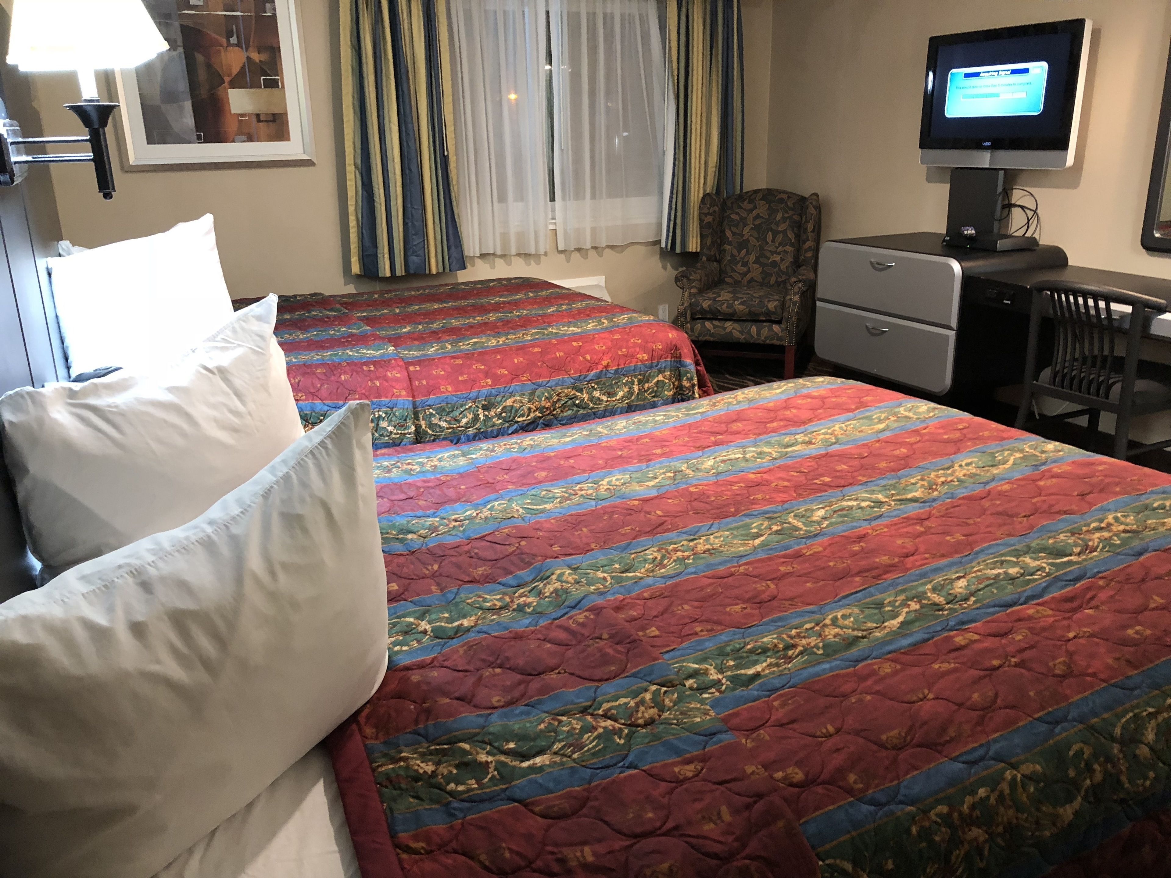 Una habitación de hotel con dos camas, un escritorio, una silla, un televisor y una ventana con cortinas.