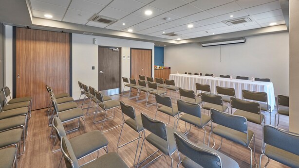 Een vergaderzaal met rijen stoelen, een lange tafel en een projectiescherm.