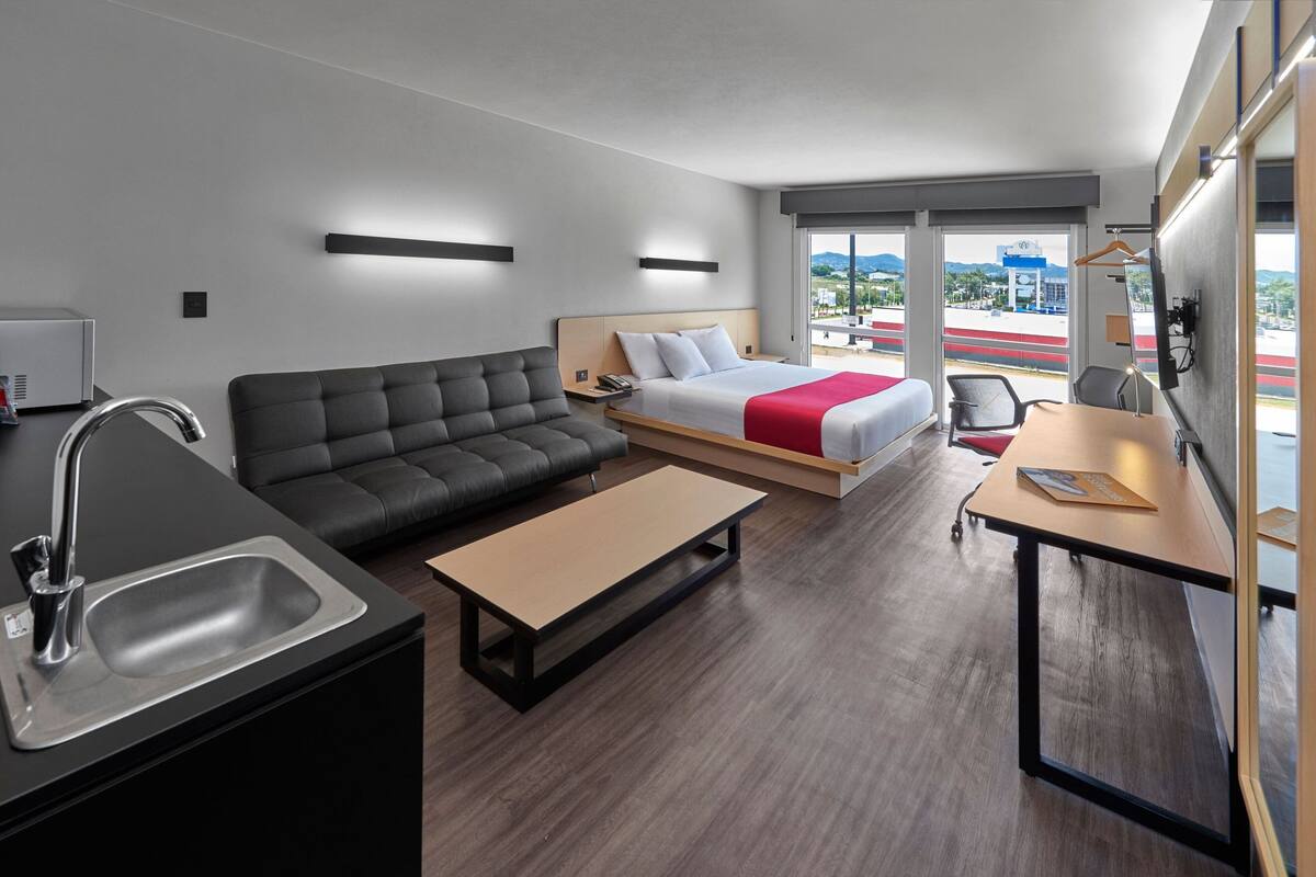Una habitación de hotel moderna con sofá, cama, escritorio, lavamanos y vista a la ciudad.