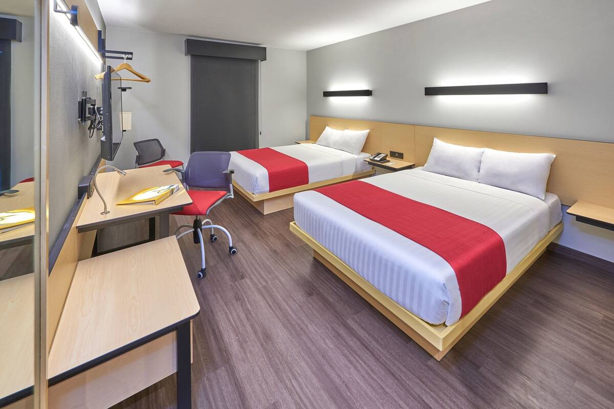 Habitación de hotel con dos camas, un escritorio, una silla, un televisor y un armario.