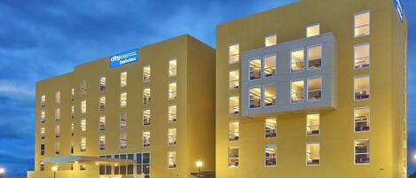 Ein City Express Hotel mit einer modernen, gelben Fassade, mehreren Stockwerken und einem Van vor der Einfahrt.