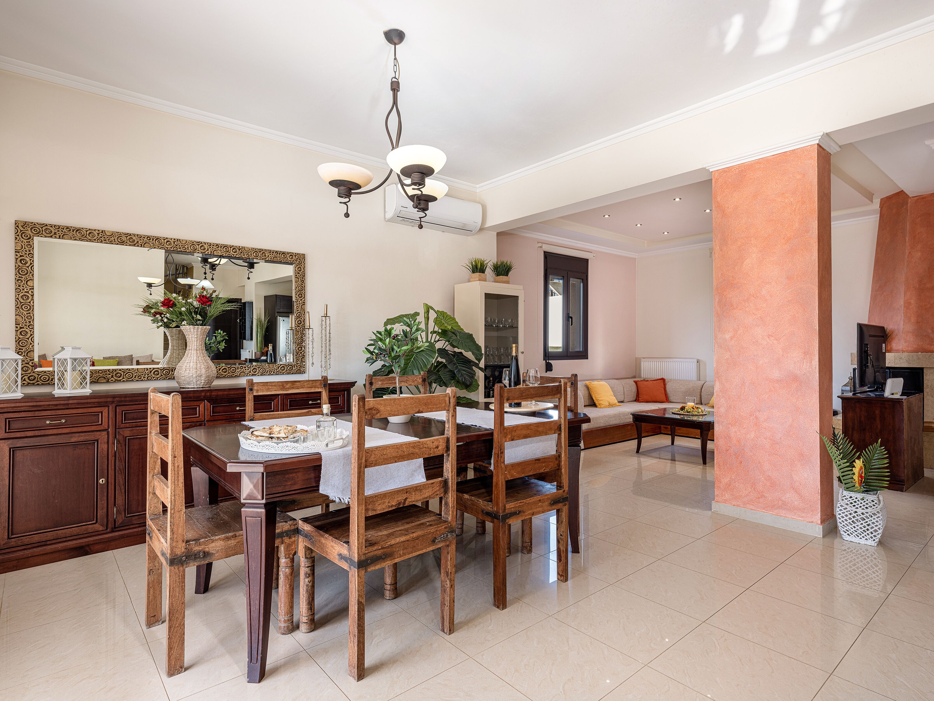 A spacious living area with a dining table, wooden chairs, a sofa, and a large mirror.