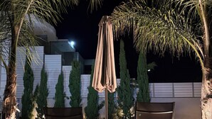 An outdoor seating area with two chairs and a table, surrounded by palm trees and a pool. - Villa Fanouris (Chania)