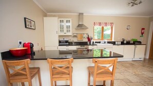 A kitchen with a central island, wooden chairs, and a window with curtains. - The Stables 10037 (Lismullin)