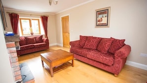 A living room with two red sofas, a wooden coffee table, and a fireplace. - The Stables 10037 (Lismullin)