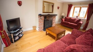 A living room with a television, fireplace, red sofa, and wooden coffee table. - The Stables 10037 (Lismullin)
