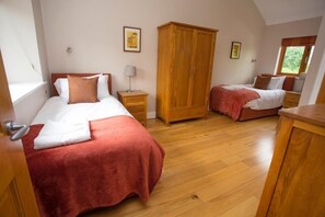Dormitorio con dos camas, armario de madera y ventana con vista a la vegetación.