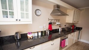 Une cuisine avec des armoires blanches, un comptoir noir, une hotte de cuisinière en acier inoxydable et une horloge au mur.