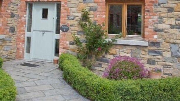 Une maison en pierre avec une porte centrale, une petite fenêtre et un chemin menant à l’entrée.