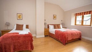 Une chambre avec deux lits, un plancher en bois et une fenêtre agrémentée d’une lambrequin à rayures.