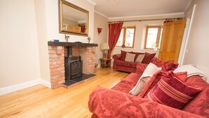 A living room with a brick fireplace, a red patterned sofa, and a wooden floor. - The Hen House 10065 (Lismullin)