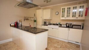 A kitchen with a central island, white cabinets, a microwave, and a clock on the wall. - The Hen House 10065 (Lismullin)