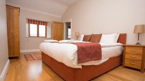 A bedroom with a large bed, wooden flooring, a window with curtains, a nightstand, and a lamp. - The Hen House 10065 (Lismullin)