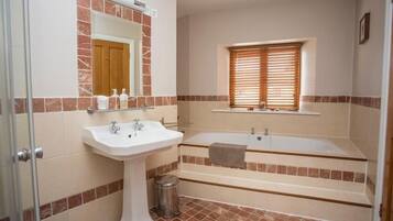 Un baño con lavamanos pedestal, bañera y ventana con persianas.