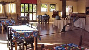 Un comedor espacioso con múltiples mesas y sillas, amplias ventanas que dejan entrar luz natural, y un techo rústico con vigas a la vista.