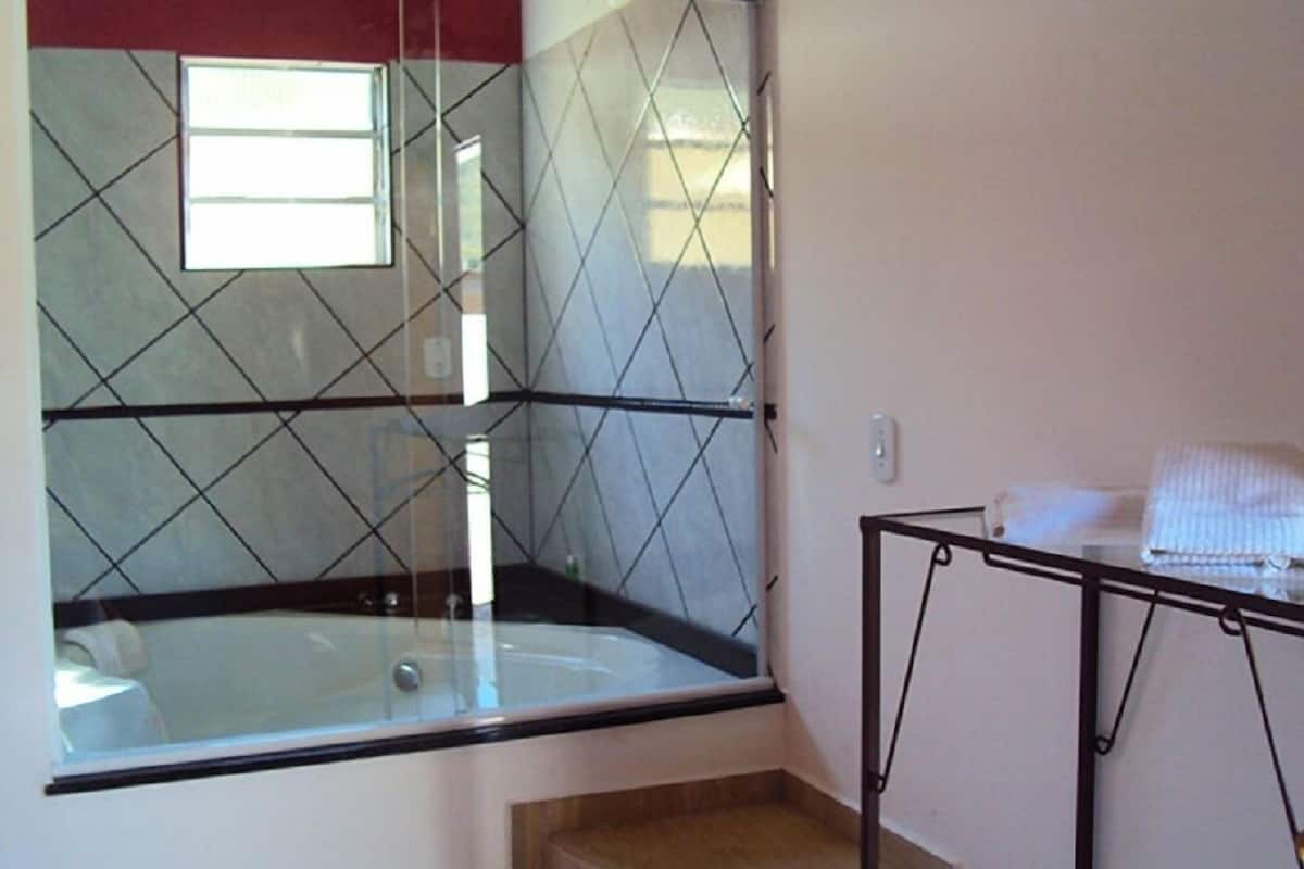 A bathroom with a glass-enclosed jacuzzi, a small wooden bench, and a metal rack with towels.