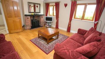 Una sala de estar con chimenea, cortinas rojas, una mesa de centro de madera y un sofá rojo.