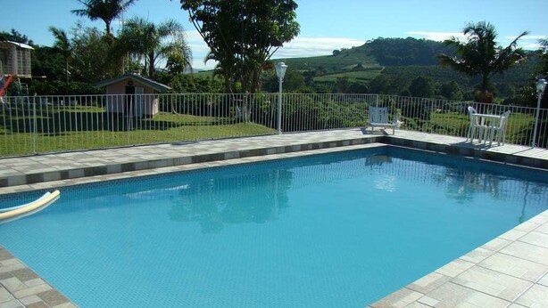 A rectangular swimming pool with a tiled deck, surrounded by a white fence.
