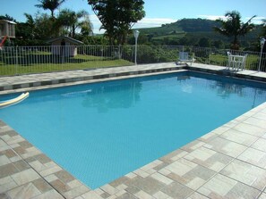 A rectangular swimming pool with a tiled deck, surrounded by a white fence. - Pousada Primavera da Serra (Serra Negra)